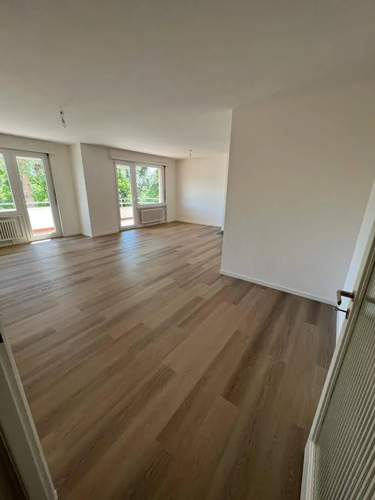 Le même séjour après travaux : murs blancs et sol neuf.