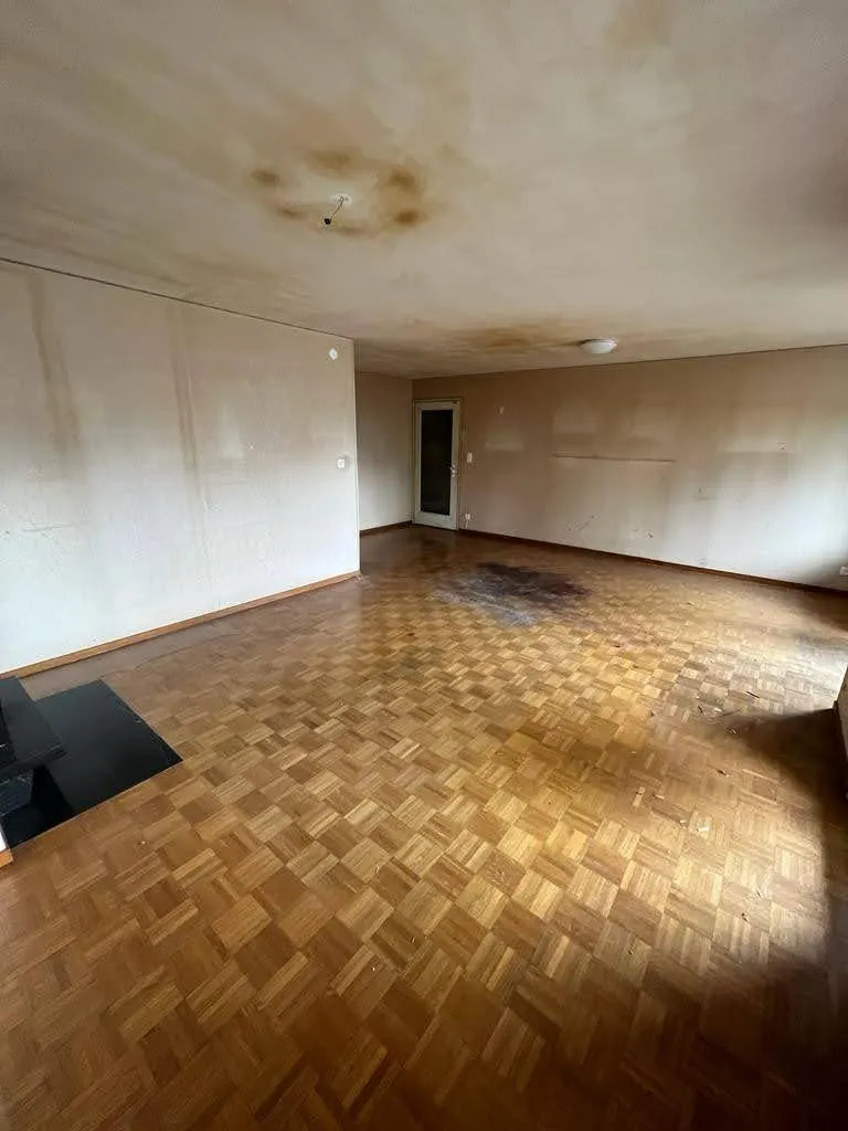 Séjour avant travaux : plafond taché, murs jaunis et parquet ancien.