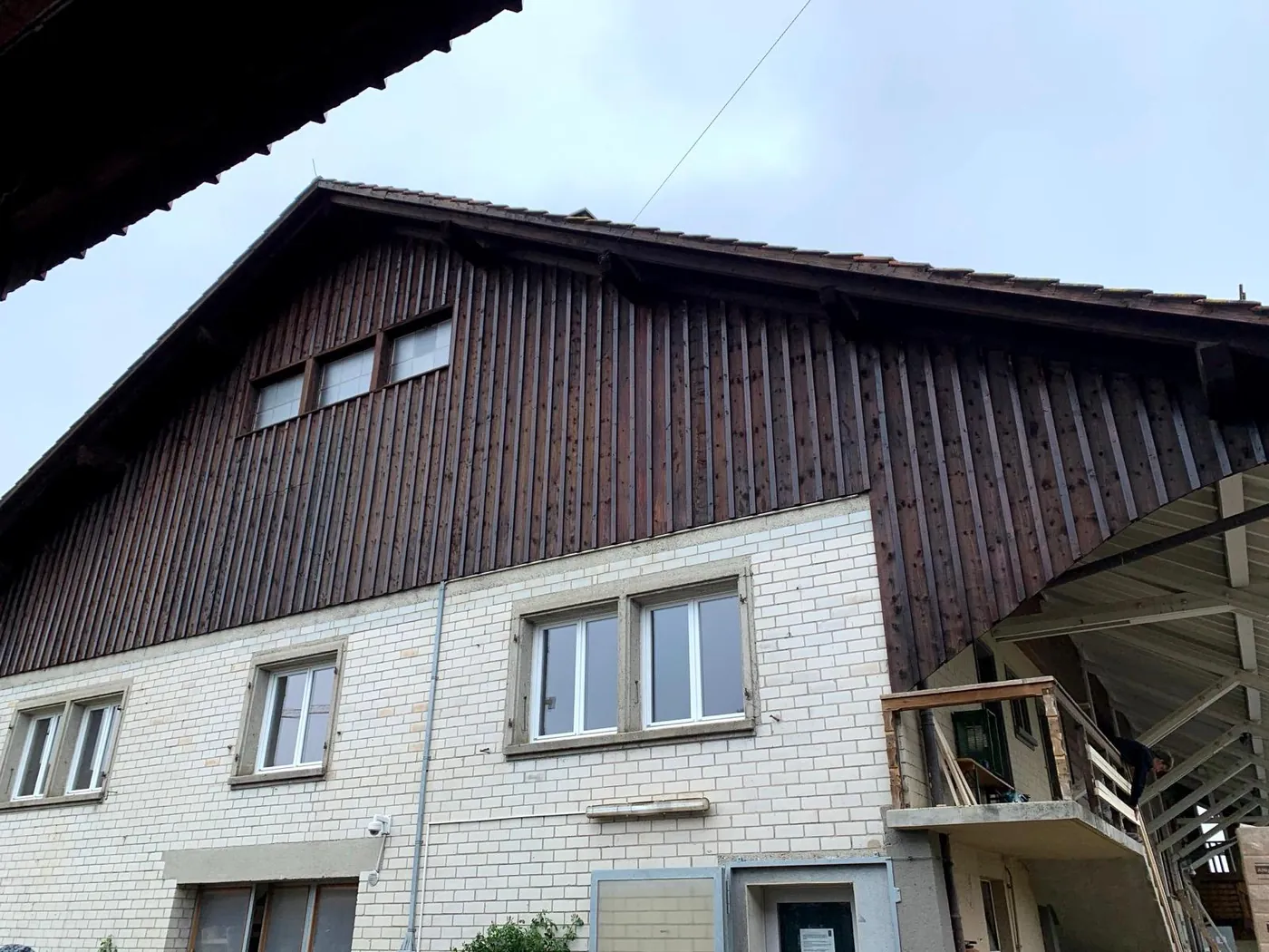 Ferme avant travaux : soubassement en briques grises et bardage bois foncé.
