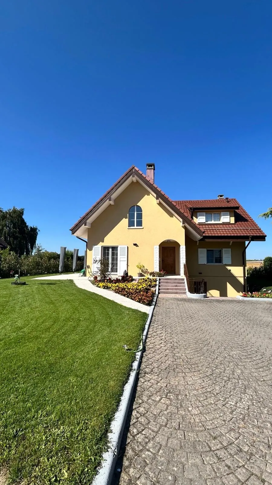 Villa jaune avec allée pavée et pelouse.